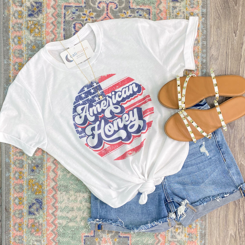 Retro 'American Honey' White Circle Flag Tee-This tee shirt is as sweet as honey! The retro style lettering 'American Honey' graphic over a vintage distressed American flag design. Perfect for all the Patriotic holidays or any day! -Cali Moon Boutique, Plainville Connecticut